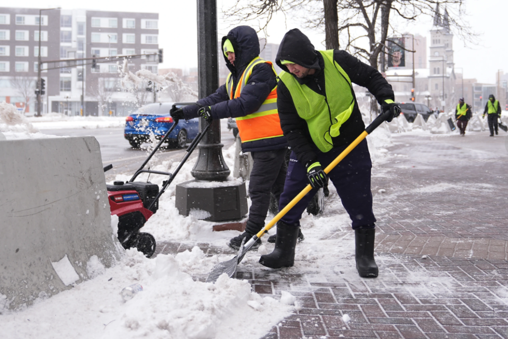 Workers clear snow off the ground Sunday March 15 2026 in St. Paul Minn